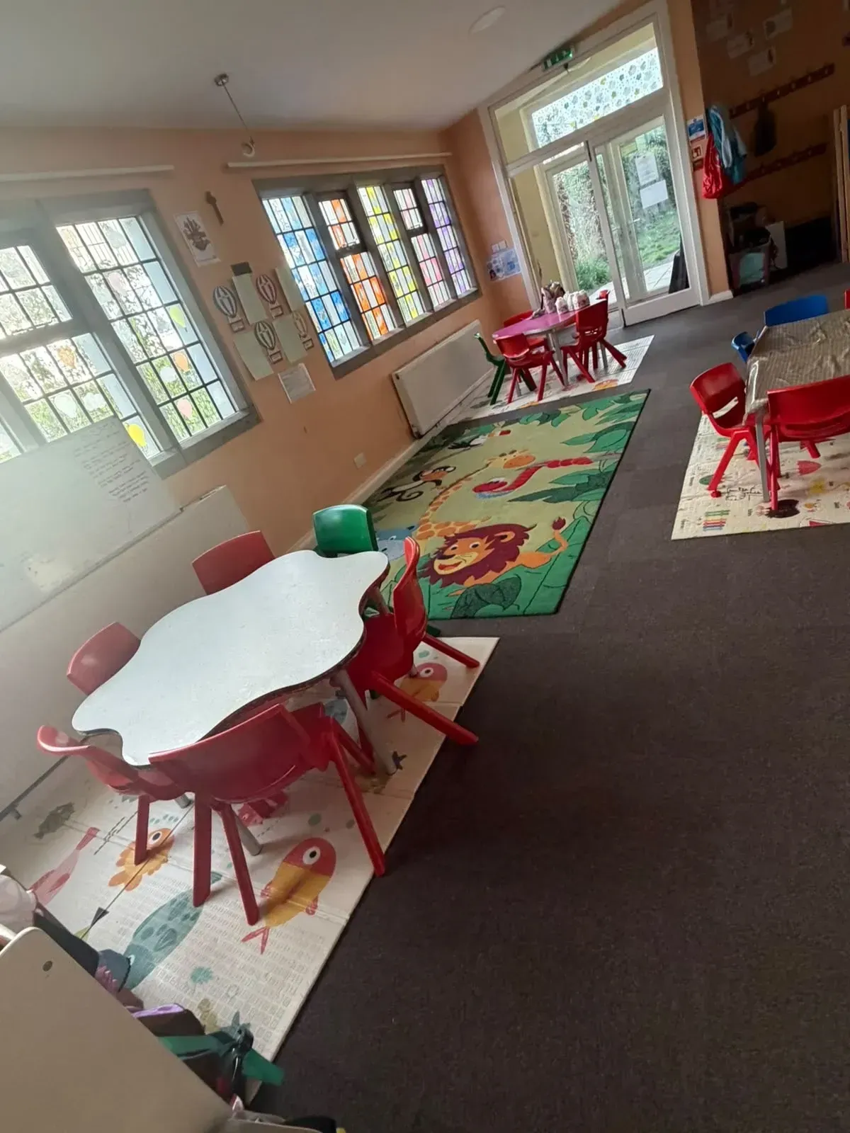 Nursery and preschool room with play tables, a jungle rug and colourful window art at St Peters Church, Milton